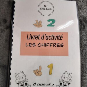 Peut inclure: Un livret d'activité à reliure spirale intitulé N.c Créa book Livret d'activité LES CHIFFRES. La couverture présente le chiffre 2 avec un geste de la main, le chiffre 1 avec un geste de la main, deux illustrations de chats et le texte 3 ans et +.