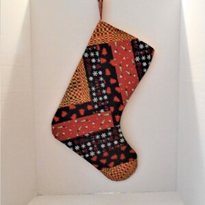 May include: A red, black, and gold Christmas stocking with a patchwork design featuring various holiday patterns, including snowflakes, Christmas trees, and geometric shapes.