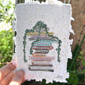 May include: Watercolor illustration on textured paper of a stack of books with a small potted plant on top and trailing vines. The books are various colors, and the plant is green. The paper has a deckled edge.