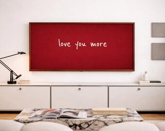 Könnte beinhalten: Ein modernes Wohnzimmer mit einem großen, rot gerahmten Kunstwerk mit dem weißen Schriftzug "love you more". Darunter ein weißer Schrank, ein Marmor-Couchtisch und eine schwarze Schreibtischlampe.
