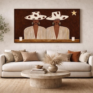 Puede incluir: Una obra de arte enmarcada representa dos figuras con sombreros blancos con lunares negros y blazers a rayas. Una estrella dorada está encima de las figuras. La obra cuelga sobre un sofá blanco con cojines y una mesa de centro redonda.