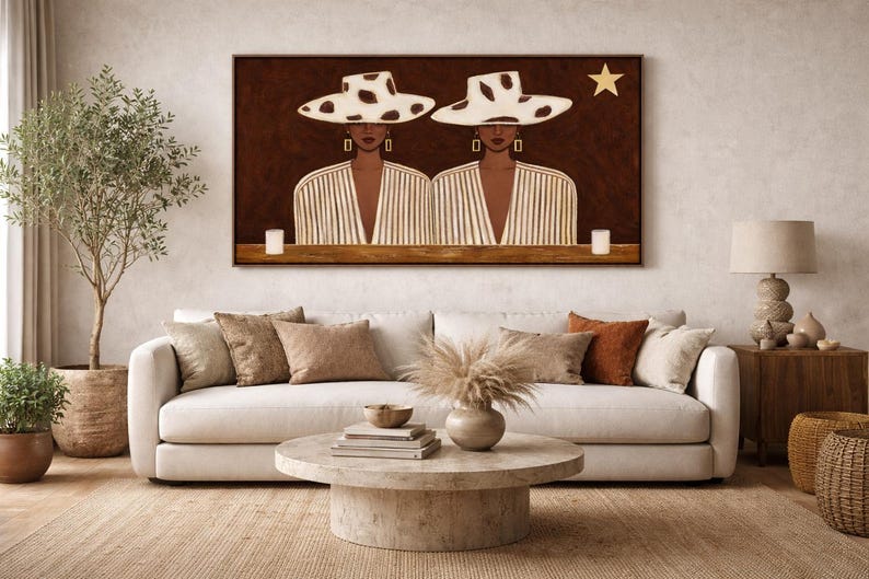 May include: A framed artwork depicts two figures wearing white hats with black spots and striped blazers. A gold star is above the figures. The artwork hangs above a white sofa with decorative pillows and a round coffee table.