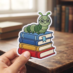 May include: An embroidered patch featuring a green caterpillar with round glasses resting on a stack of four books. The books are colored blue, dark blue, yellow, and red, with a light blue bookmark hanging from the top blue book.