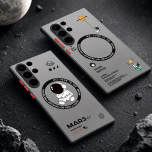Può includere: Due custodie grigie per telefono a tema spaziale. Ogni custodia presenta un'illustrazione di un astronauta, il testo "WELCOME TO THE MOON" e altre grafiche a tema spaziale. Una custodia ha la parola "MARS" e l'altra il testo "EXPLORE DISCOVERY".