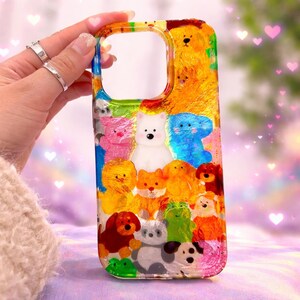 May include: A vibrant phone case adorned with cartoon dogs in diverse colours. The case has a clear border with a rainbow gradient. The dogs include brown, white, blue, pink, and yellow. The case is designed to fit a smartphone.