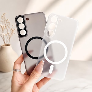 May include: Two phone cases are displayed, one grey and one translucent. The grey case features a black circle and a camera array. The translucent case has a white circle and a camera array. Both cases are designed for a smartphone.