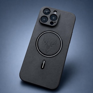 May include: Black phone case with a deer head emblem and a circular design. The case has a matte finish and a built-in charging port. The phone case is designed to fit a smartphone with multiple camera lenses.