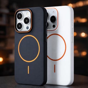 Op de afbeelding: Twee telefoonhoesjes, één zwart en één wit, worden naast elkaar getoond. Beide hoesjes hebben een oranje cirkelvormig ontwerp op de achterkant en oranje accenten rond de camera. De hoesjes zijn ontworpen om de telefoon te beschermen.