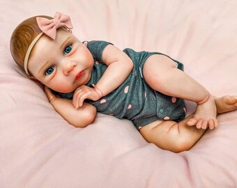 May include: A realistic baby doll with blue eyes, wearing a grey and white polka dot onesie and a pink bow headband.