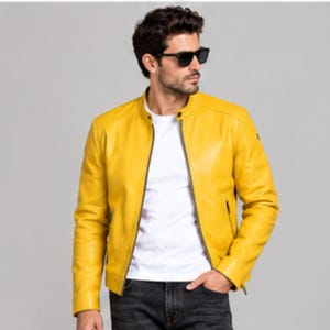 Peut inclure: Une veste en cuir jaune vif dotée d'un col montant, d'une fermeture éclair centrale sur le devant et de deux poches latérales zippées. La veste est portée sur un t-shirt blanc uni et associée à un jean en denim gris foncé.