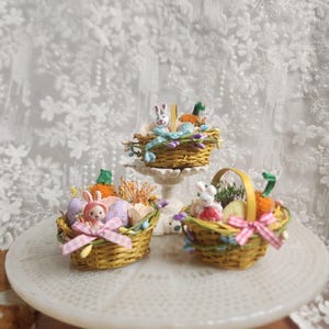 May include: Three miniature Easter baskets filled with decorative items. Each basket is woven with a yellow hue and contains small bunny figurines, carrots, and pastel-colored eggs. Ribbons and floral accents add to the festive theme.