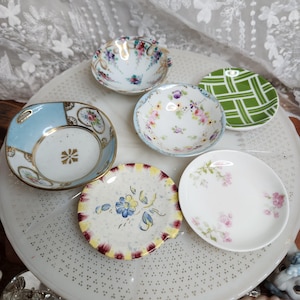 Op de afbeelding: Een verzameling van vijf kleine, ronde keramische schaaltjes met diverse ontwerpen. Eén schaaltje heeft een lichtblauwe rand met gouden accenten, een ander een groen-wit ruitpatroon en drie tonen delicate bloemmotieven in roze, blauw en geel.