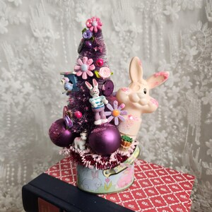 Composizione stravagante con coniglietto pasquale: rosa, viola, perline vintage, albero a forma di spazzola per bottiglie.