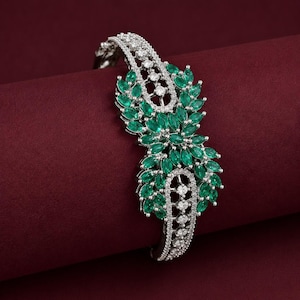 May include: A silver-toned bracelet featuring a central cluster of marquise-cut green stones arranged in a leaf-like pattern, accented by small round clear stones set along the band and the decorative centerpiece in a symmetrical design.