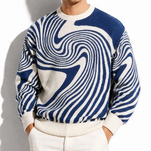 Könnte beinhalten: Ein Rundhals-Pullover mit einem einzigartigen blau-weißen Wirbelmuster. Der Pullover hat einen gerippten Saum und Bündchen, und das Design bedeckt das gesamte Kleidungsstück. Das Farbschema ist ein auffälliger Kontrast.