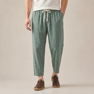 Könnte beinhalten: Salbeigrüne Hose mit lockerer Passform, geradem Beinverlauf und einem elastischen Bund mit weißem Kordelzug. Die Hose besteht aus einem strukturierten Stoff und wird mit dunkelbraunen Ledersneakern kombiniert.
