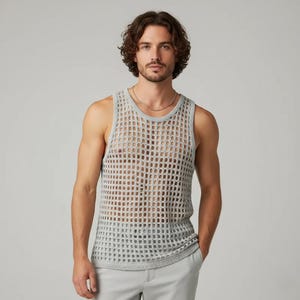 Könnte beinhalten: Ein hellgraues Tanktop mit offenem Gewebe. Das ärmellose Oberteil hat einen runden Ausschnitt und ein lockeres, atmungsaktives Design. Das Tanktop besteht aus einem weichen Strickmaterial. Das Model trägt eine silberne Halskette und hellgraue Hosen.