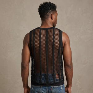 May include: Black mesh tank top with vertical stripes. The sleeveless shirt has a round neckline and a see-through design. The garment is worn over a black undershirt and paired with blue jeans.