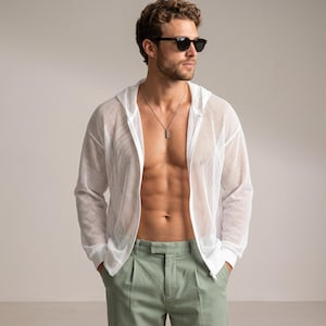 May include: A white long-sleeve zip-up hoodie made of a sheer mesh fabric with a hood and ribbed cuffs. The garment is worn open over a bare torso, paired with light green trousers. A silver chain necklace with a rectangular pendant is visible.