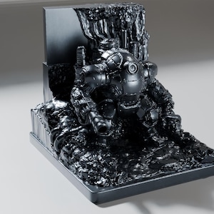 May include: A dark gray, detailed sculpture of a futuristic robot warrior. The robot is mounted on a rectangular base with a textured, rocky terrain. The sculpture has a metallic sheen and is set against a neutral background.