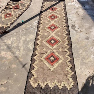 May include: Two matching runner rugs with a geometric diamond pattern. The rugs feature a brown and tan background with red and black diamond shapes. The edges are dark brown with a zig-zag design. One rug has a fringe.