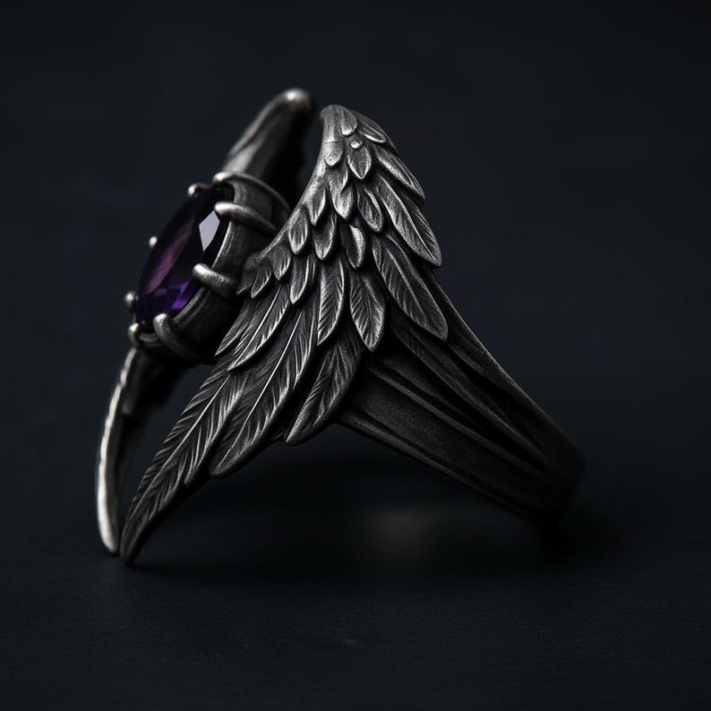 Puede incluir: Anillo plateado con una gema de amatista y dise&ntilde;o de alas de &aacute;ngel detalladas. Las alas presentan detalles de plumas, creando una est&eacute;tica g&oacute;tica o fant&aacute;stica. El anillo se encuentra sobre un fondo oscuro.