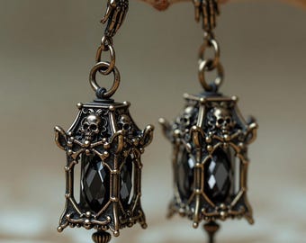 Brincos góticos em formato de lanterna com caveira e pingente de cristal preto em tom bronze.