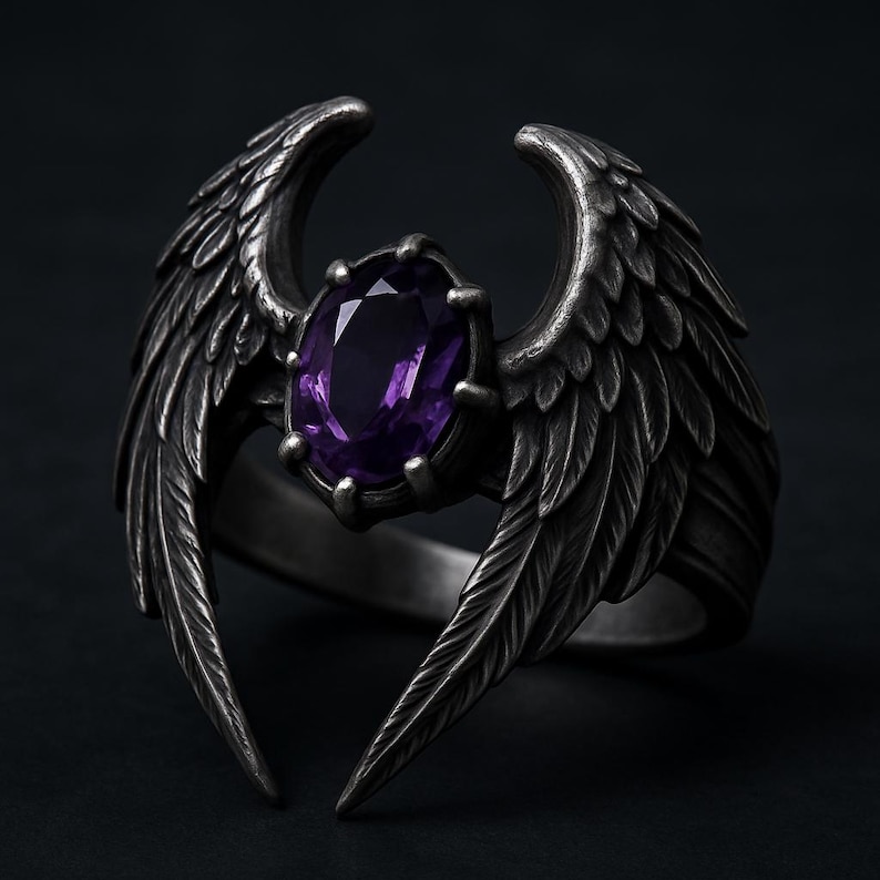 Puede incluir: Anillo plateado con una gema p&uacute;rpura ovalada. El dise&ntilde;o del anillo incluye alas estilizadas y detalladas que se curvan alrededor de la gema, creando una est&eacute;tica g&oacute;tica &uacute;nica. El anillo se presenta sobre un fondo oscuro.