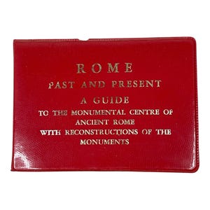May include: A red guide titled "ROME PAST AND PRESENT" with gold lettering. The guide is a travel book about the monumental center of ancient Rome, including reconstructions of the monuments.