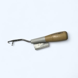 May include: A Wonderart latch hook tool with a wooden handle and a metal hook. The handle is light brown and gray, with the Wonderart logo printed on it. A small tag is attached to the tool.