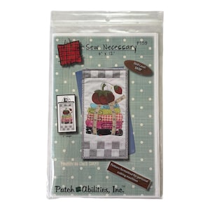 Op de afbeelding: Een naaipatroon getiteld "Sew Necessary" in een doorzichtige plastic verpakking. Het patroon heeft een kleurrijk ontwerp van opgestapelde stoffen, tomaten en een meetlint. De verpakking meet 15,24 cm x 30,48 cm.