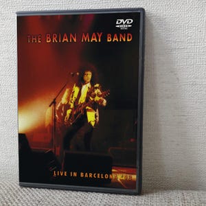 以下が含まれることがあります： 「The Brian May Band Live in Barcelona 2003」のDVDケース。カバーには、ステージでギターを演奏するミュージシャンのライブパフォーマンス写真が写っており、バンド名が大きく表示されています。