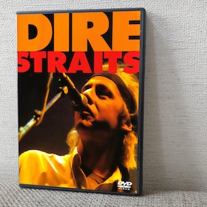 May include: DVD case for Dire Straits. The cover features the band's name in large orange and red letters. A close-up image of a man singing into a microphone is visible. The DVD case has a black border and the DVD logo is in the bottom right corner.