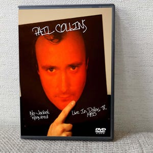 以下が含まれることがあります： フィル・コリンズのDVDケース。テキスト「Phil Collins」は白い文字です。カバーアートは、指を指しているフィル・コリンズの赤みがかった画像です。ケースのテキストは「No Jacket Required」と「Live In Dallas, TX. 1985」です。