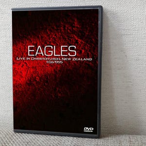 Op de afbeelding: DVD-hoesje voor het Eagles-concert "Live in Christchurch, New Zealand". De cover toont de bandnaam in witte blokletters tegen een rood-zwarte achtergrond met textuur. De dvd-hoes is zwart.
