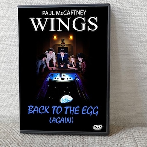 以下が含まれることがあります： ポール・マッカートニー＆ウィングスのアルバム「Back to the Egg (Again)」のDVDケース。カバーには、ピンボール台の周りに集まったバンドメンバーが描かれており、背景は暗く、バンド名は白で表示されています。