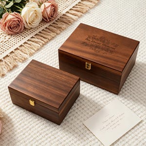 Puede incluir: Dos cajas de recuerdos de madera con acabado marrón oscuro. La caja más grande tiene grabadas las palabras "Our Shared Memories" y detalles florales. Ambas cajas tienen cierres dorados. Una tarjeta con texto manuscrito descansa cerca.