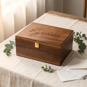May include: A wooden anniversary keepsake box with a gold clasp. The box is engraved with the names "Daniel & Rachel HERMLE" and "ANNIVERSARY December 7th, 2025" along with floral and bird designs. The box is sitting on a white tablecloth.