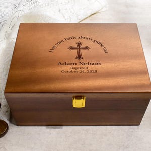 May include: A wooden box with a gold clasp, engraved with a cross and the words "May your faith always guide you." The box is personalized with a name and baptism date. Two wooden crosses are on the sides.