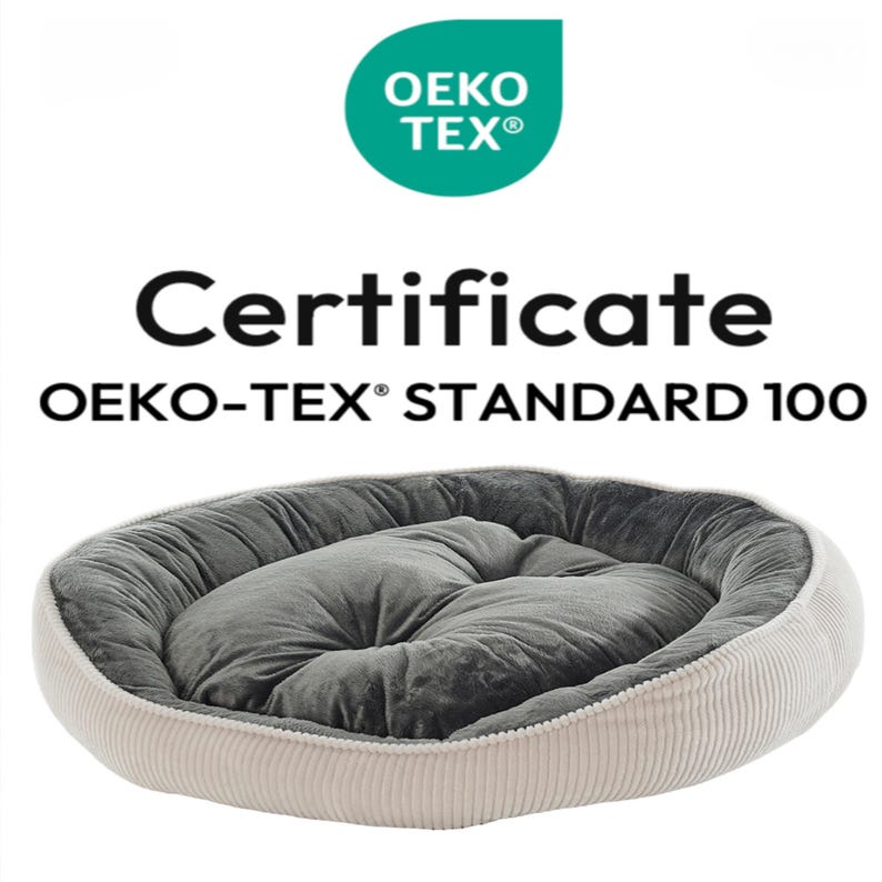 May include: A plush, oval pet bed with a gray interior and a cream-colored corduroy exterior. The bed is labeled with the text "Certificate OEKO-TEX&reg; STANDARD 100" and the OEKO-TEX logo, indicating it meets specific safety standards.