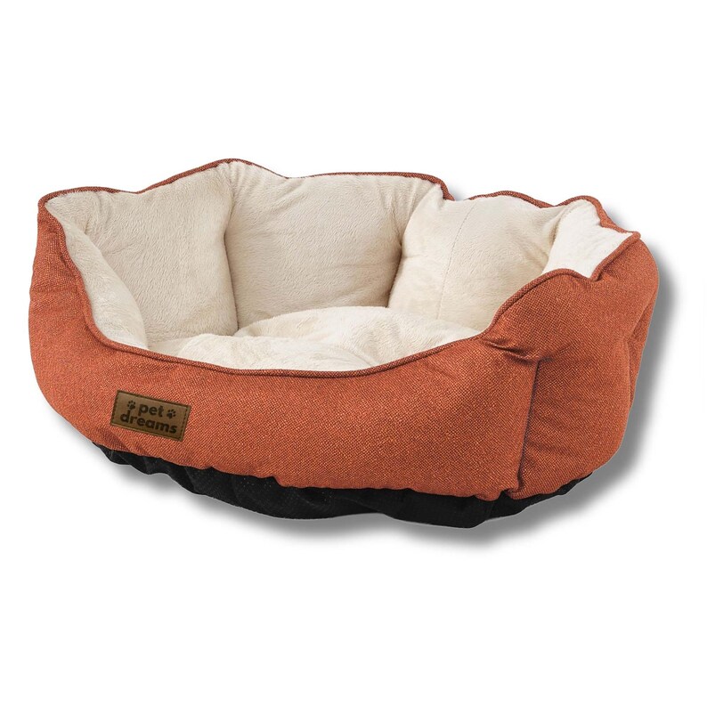 Op de afbeelding: Een hondenmand met een roestkleurige buitenkant en een zacht, cr&egrave;mekleurig interieur. Het bed heeft een afgeronde vorm met opstaande randen en een zwarte basis. Een klein, bruin label met de tekst "pet dreams" is zichtbaar.