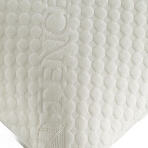 Puede incluir: Primer plano de una esquina de colch&oacute;n blanco con un patr&oacute;n texturizado y punteado. La palabra "ZEN" est&aacute; grabada en la superficie. La esquina es redondeada y la tela parece suave y c&oacute;moda.