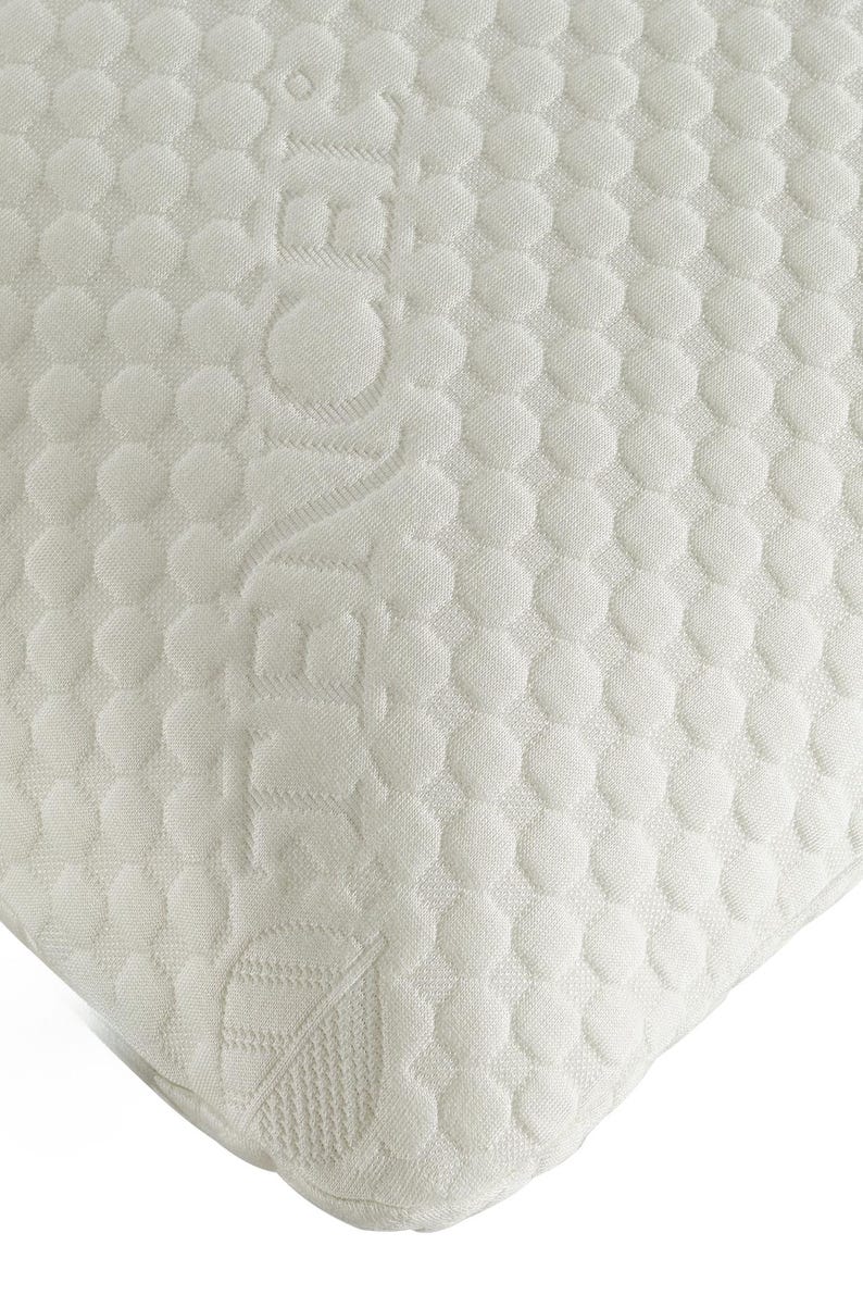 Puede incluir: Primer plano de una esquina de colch&oacute;n blanco con un patr&oacute;n texturizado y punteado. La palabra "ZEN" est&aacute; grabada en la superficie. La esquina es redondeada y la tela parece suave y c&oacute;moda.