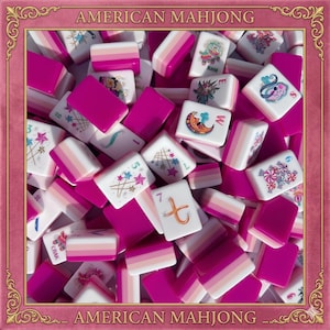 May include: A collection of American Mahjong tiles featuring a pink and white color scheme. The tiles display various colorful illustrations including stars, moons, and candy, alongside letters and numbers. The text AMERICAN MAHJONG is visible.
