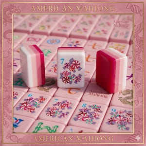 May include: A set of American Mahjong tiles in shades of pink and white. The tiles feature illustrations of colorful wrapped candies and the number 7. The set includes tiles with dragon motifs and the text American Mahjong printed on the surface.