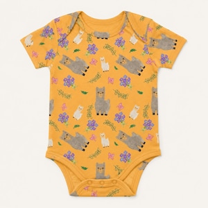 May include: A short-sleeve baby bodysuit in a mustard yellow color featuring an all-over print of grey and white alpacas, small purple flower clusters, green leafy sprigs, and tiny pink bows scattered across the fabric surface.