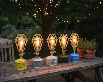 May include: Five decorative lamps with a vintage industrial design are arranged on a wooden picnic table. Each lamp features a wire cage shade, a warm glowing bulb, and a base made from repurposed propane tanks in various colors.
