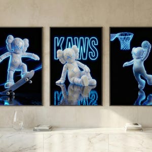 May include: Set of three framed art prints featuring a white, cartoon-like figure with blue neon outlines. One print shows the figure skateboarding, another has the word "KAWS", and the third shows the figure playing basketball. The background is black.