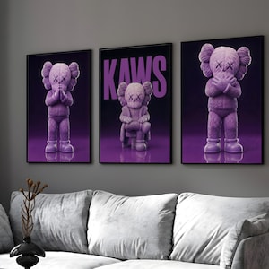 Peut inclure: Trois impressions d'art encadrées représentant des figurines KAWS violettes. Les impressions sont affichées sur un mur gris au-dessus d'un canapé gris. L'impression du milieu porte le mot "KAWS" en grandes lettres violettes. Les figurines ont des yeux barrés et les mains sur le visage.
