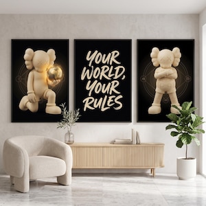 Op de afbeelding: Een set van drie ingelijste wandposters met een zwarte achtergrond. De linker- en rechterposters tonen een beige stripfiguur met X-vormige ogen. De middelste poster bevat de beige tekst "YOUR WORLD, YOUR RULES" in een penseellettertype.
